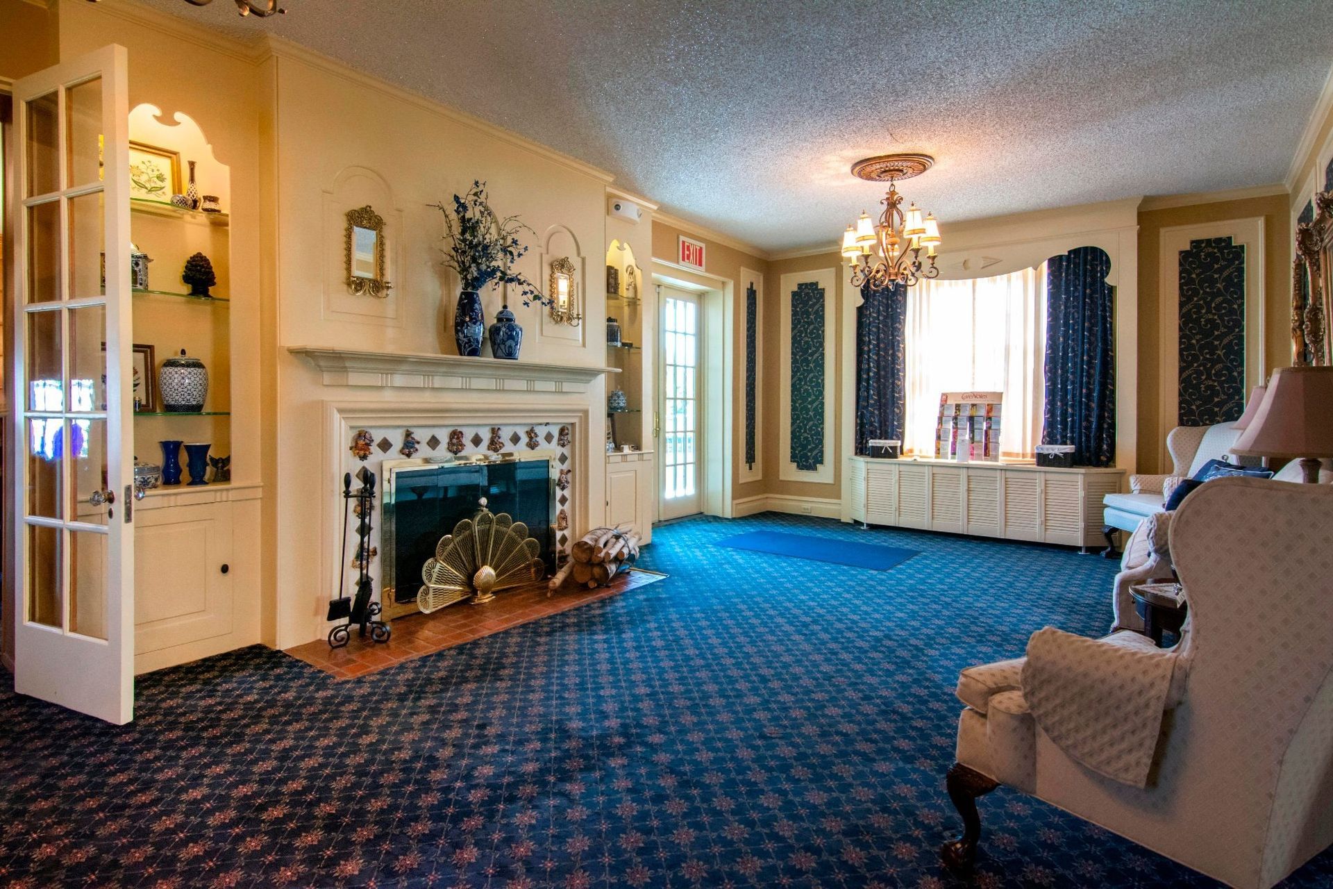 Elegant living room with blue patterned carpet, white fireplace, large windows, and a beige armchair.
