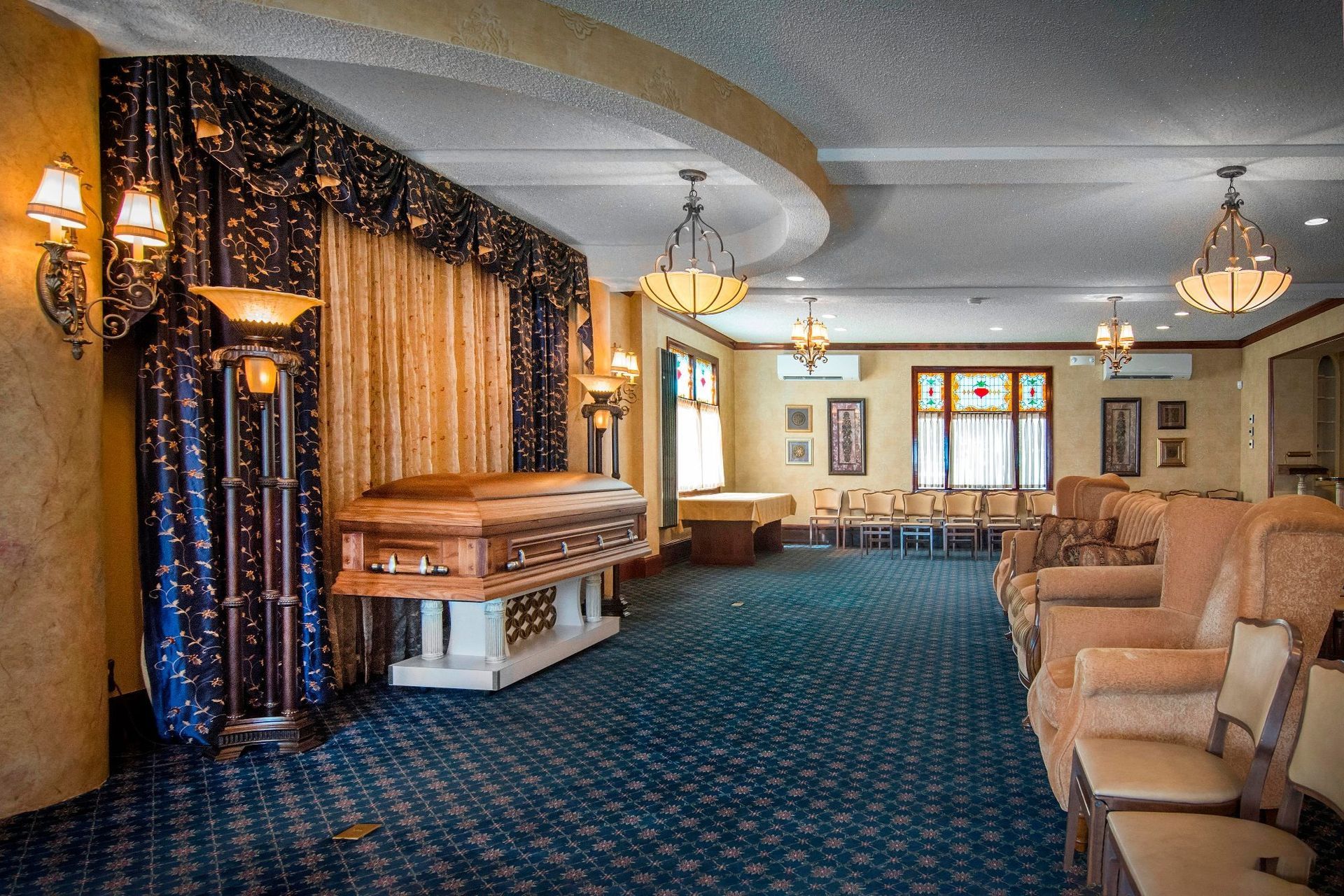 Elegant hotel lobby with blue carpet, chandeliers, curtains, and a piano in the corner