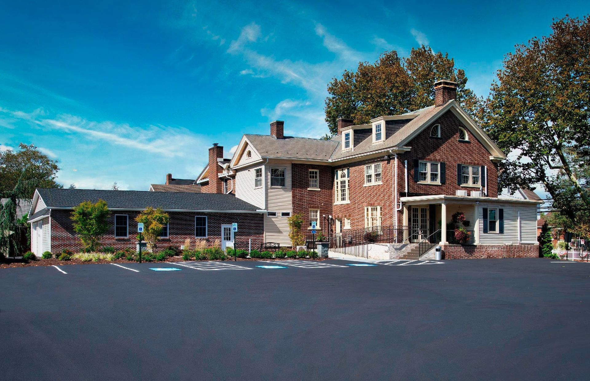 Large red-brick house with white trim and a garage, set beside a wide paved driveway under a blue sky