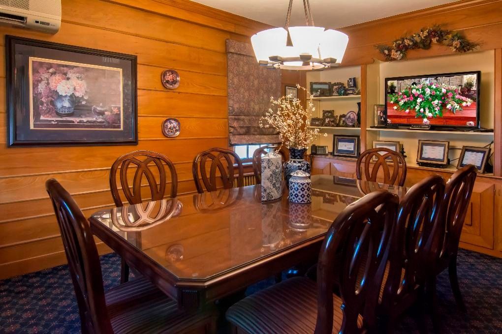Formal dining room with a large wooden table, upholstered chairs, wall art, and warm wood-paneled walls