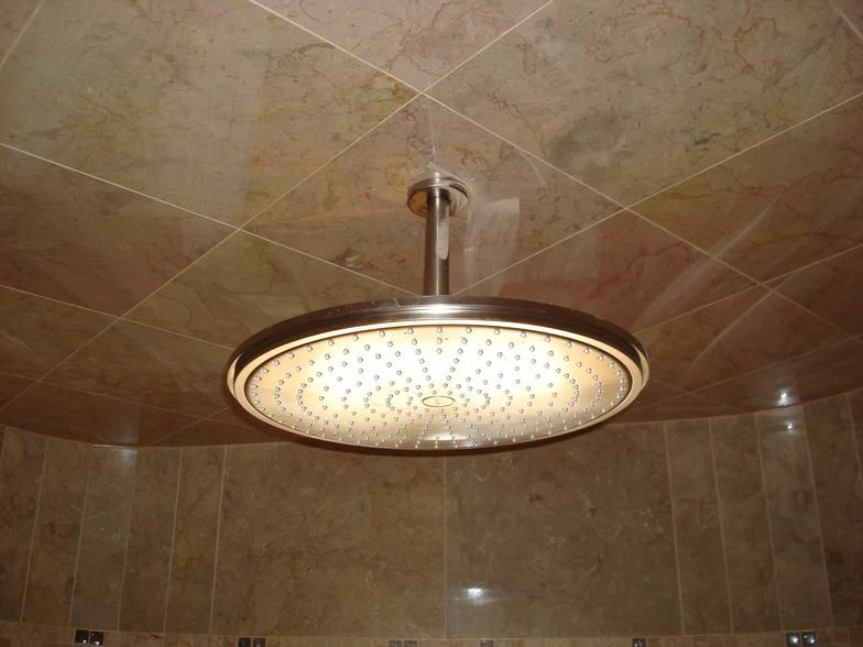 Large, round showerhead mounted on a tiled ceiling, with matching wall tiles in a beige tone.