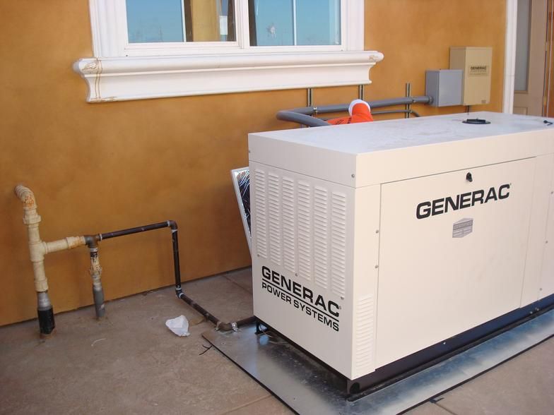 A beige Generac generator outside a building, next to a gas pipe. The wall is orange, and a window is above.