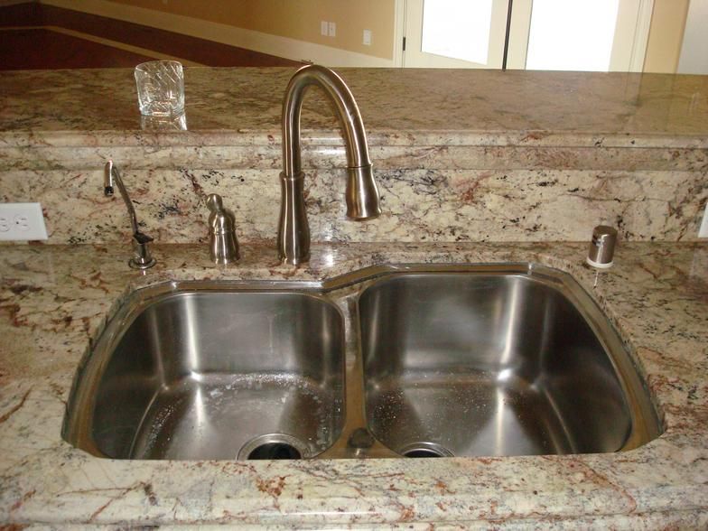A stainless steel double sink with a gooseneck faucet set into a granite countertop.