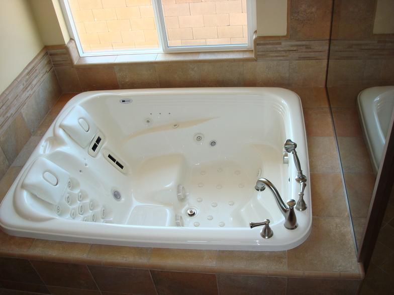 White jacuzzi tub built into a beige tile surround, with a window above.  Silver faucet and jets visible.