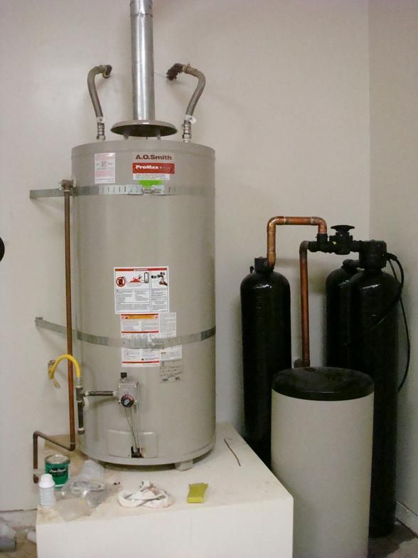 A water heater with connected pipes and two black tanks, likely for water filtration, in a utility room.