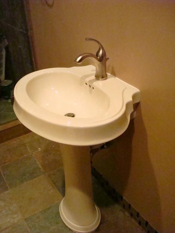 A pedestal sink in a bathroom with a chrome faucet, tan walls, and a patterned tile floor.