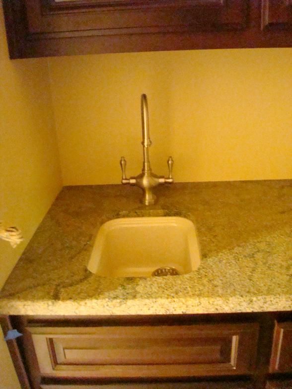 A small sink in a kitchen or bathroom. The countertop is granite, and the faucet is bronze-colored. There's dark wood cabinetry below.