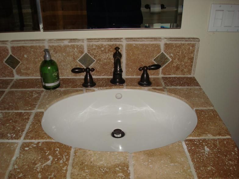 Bathroom sink with oval basin and bronze fixtures, set in a countertop with brown and beige square tiles.