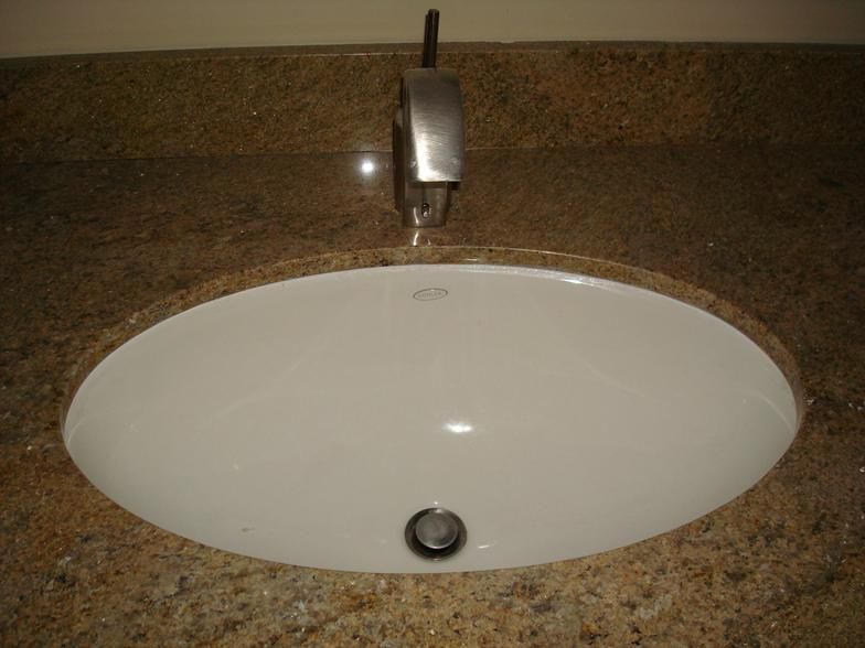 White oval bathroom sink in a granite countertop, chrome faucet.