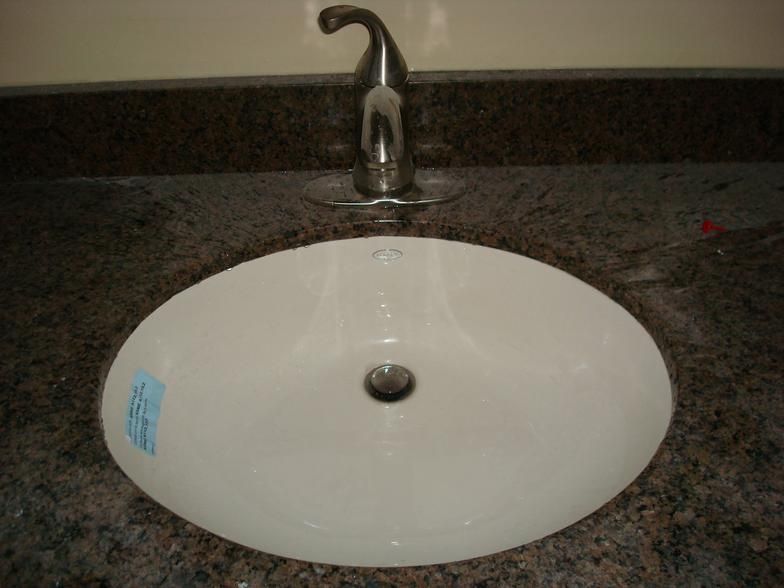 White oval bathroom sink with silver faucet on a dark granite countertop.