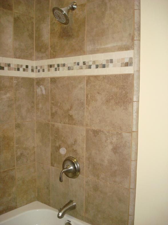 Shower with brown tile walls and a decorative mosaic border, a silver showerhead, and a faucet.
