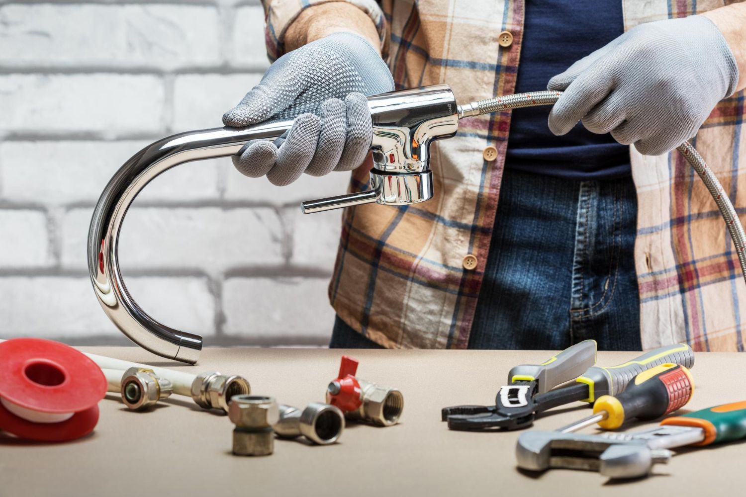 A plumber in overalls works under a sink, inspecting the pipes.