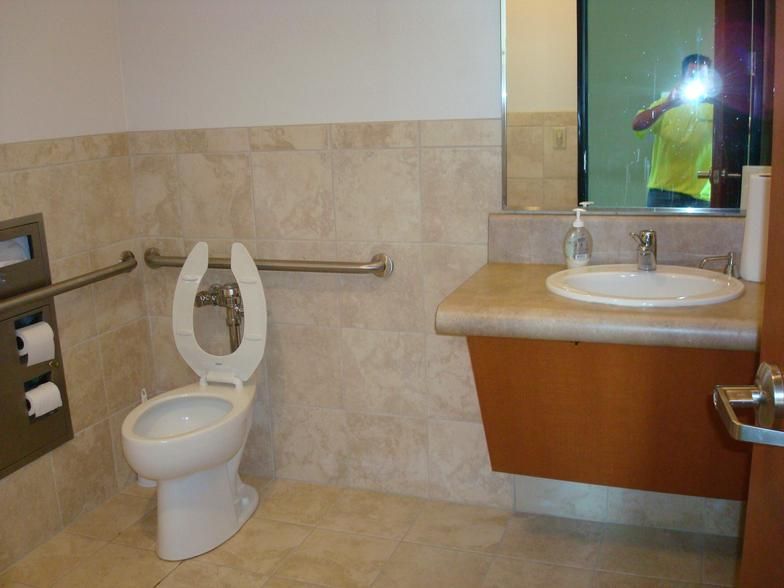 A public restroom with a toilet, sink, and mirror. The toilet has grab bars, and the sink is accessible. 