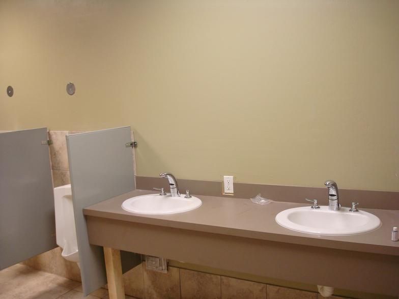 Public restroom with two sinks, stalls, and tan walls.  Gray partitions separate the sinks.