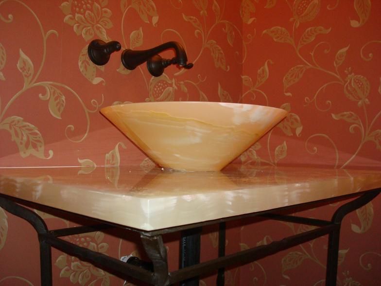 A decorative bathroom sink with an amber-colored basin on a matching countertop, set against floral wallpaper.