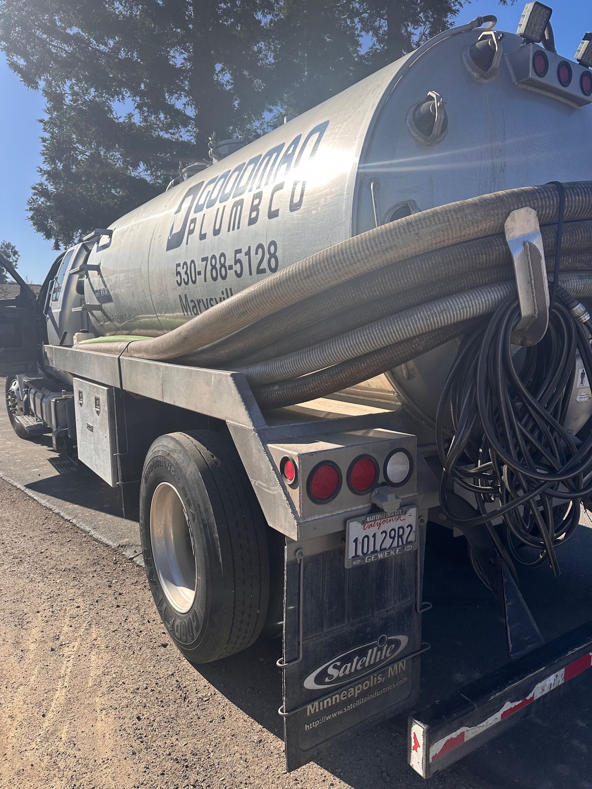 A silver septic truck parked on a gravel road, with a large tank and hose visible.