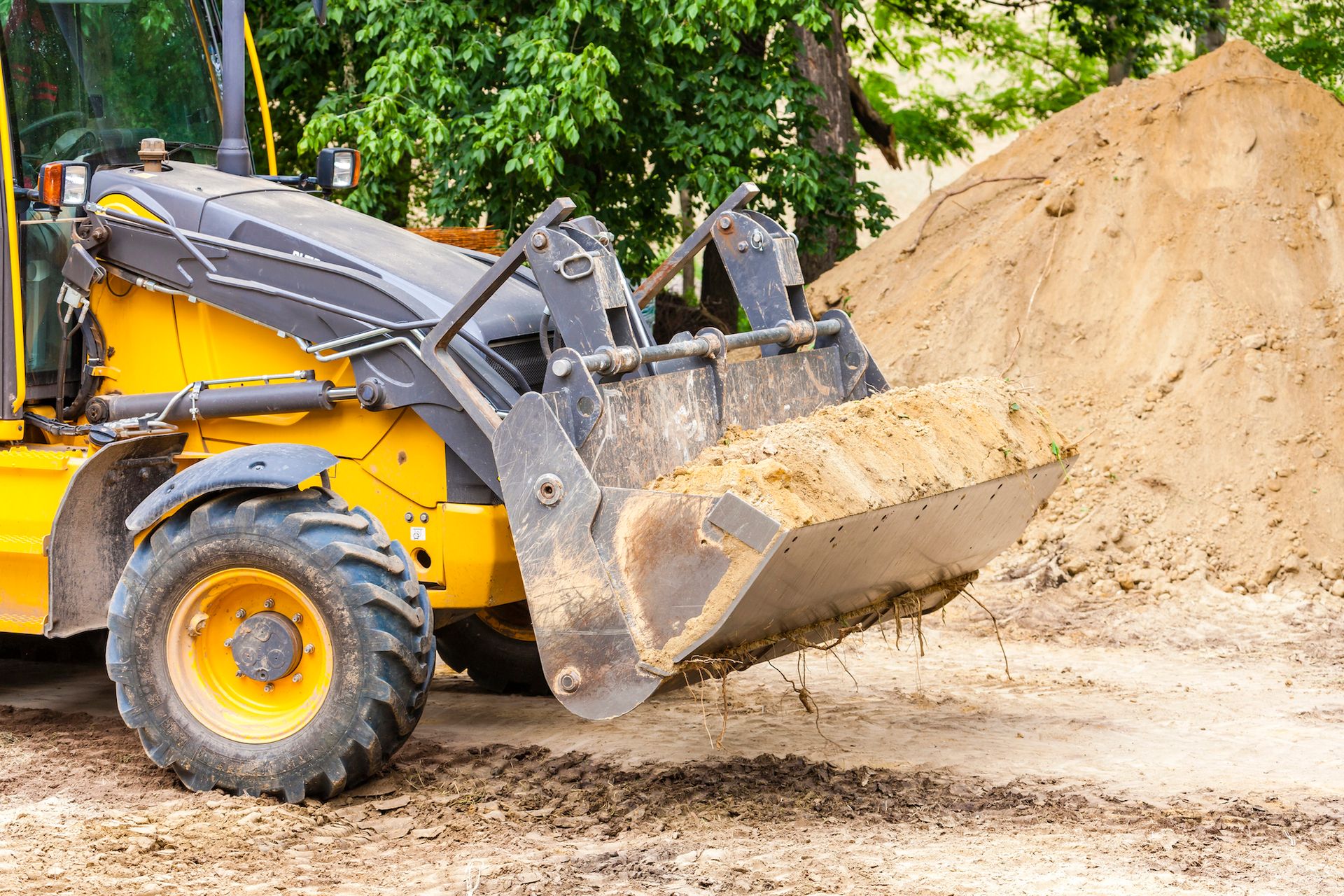 A small backhoe dumping dirt into a trench in a yard.