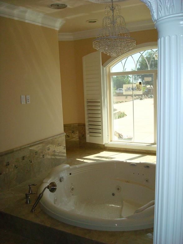 Luxurious bathroom with a jacuzzi tub, marble surround, large arched window, and a chandelier.