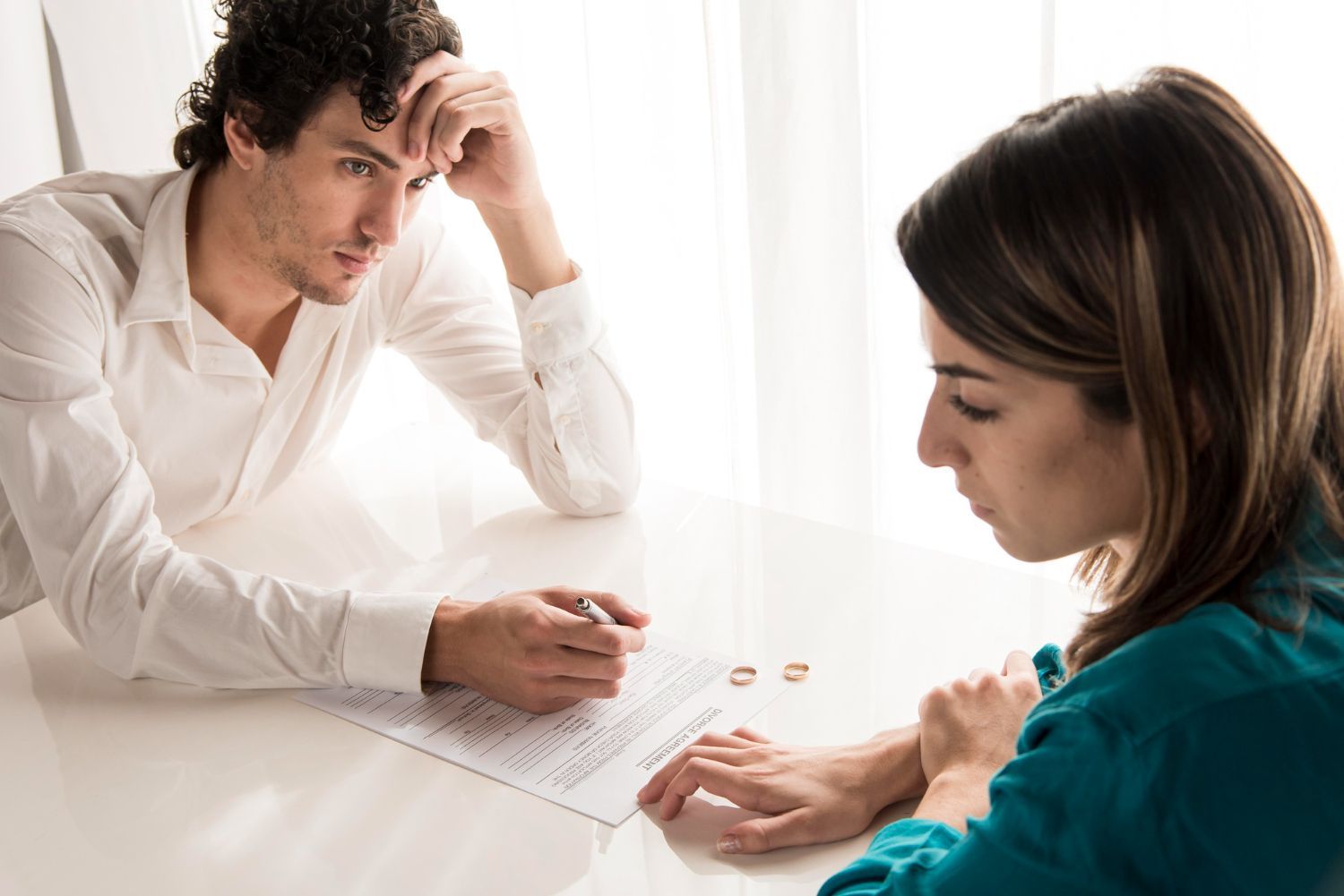 Two people discuss documents at a white table, with one pointing at a page and the other leaning in thoughtfully.