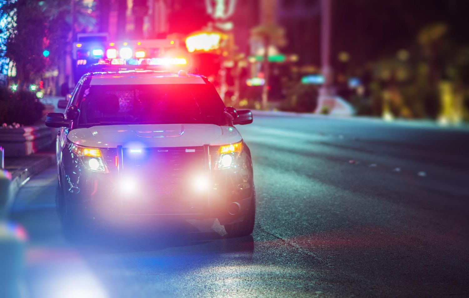 Police SUV with flashing red and blue lights on a wet city street at night