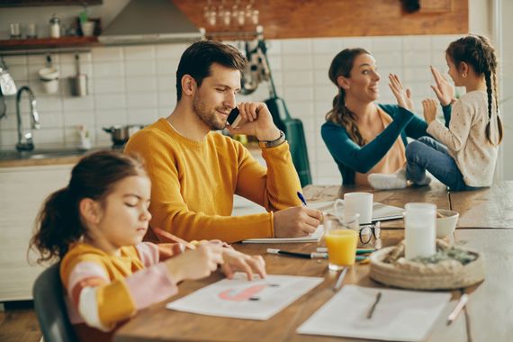 Family at a kitchen table with a child drawing and adults talking in the background