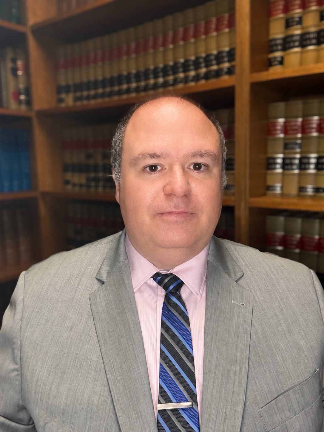 Tony Puopolo in gray suit and striped tie standing before law bookshelves in an office