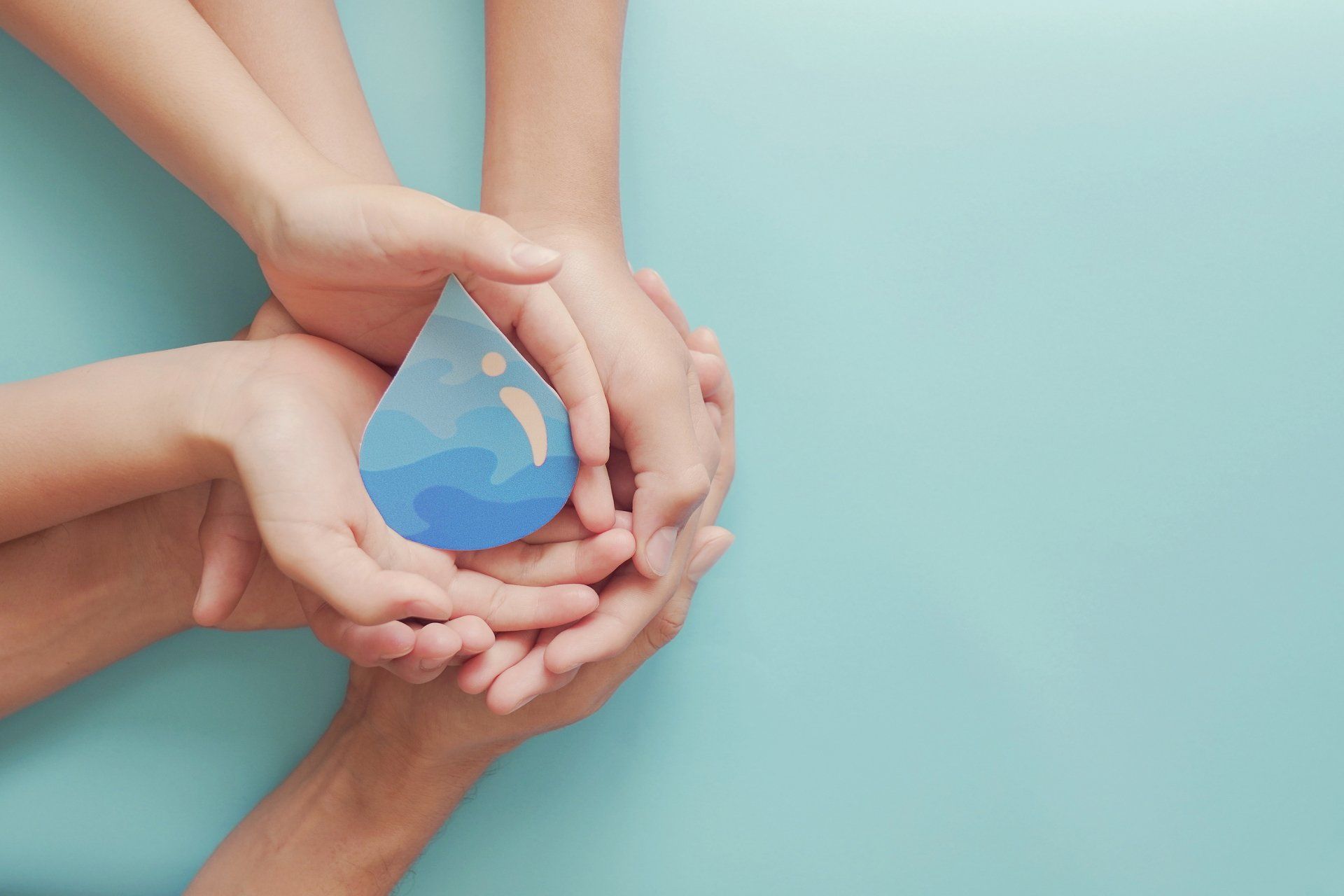 Hands cupping a blue paper water droplet against a light blue backdrop.