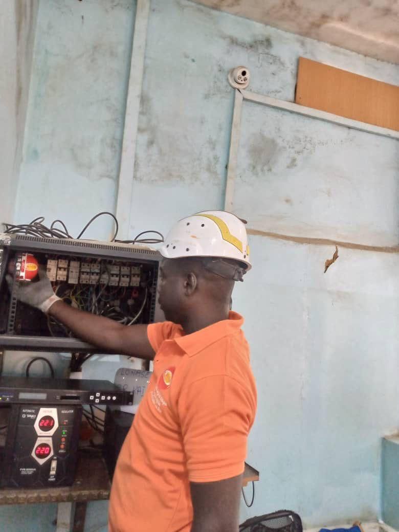 Électricien en chemise orange et casque de sécurité inspectant le panneau électrique.