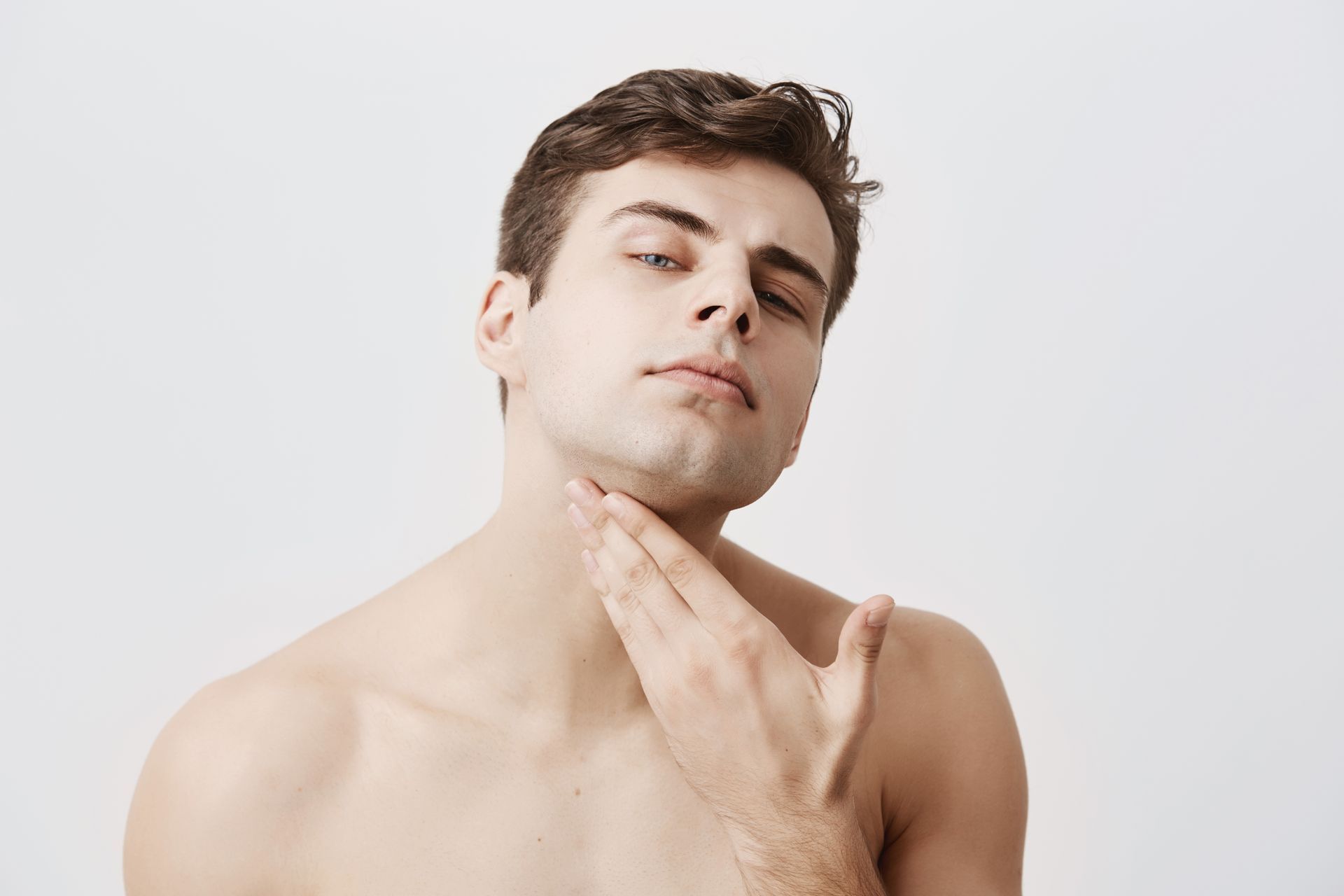 A shirtless man is shaving his neck with his hand.