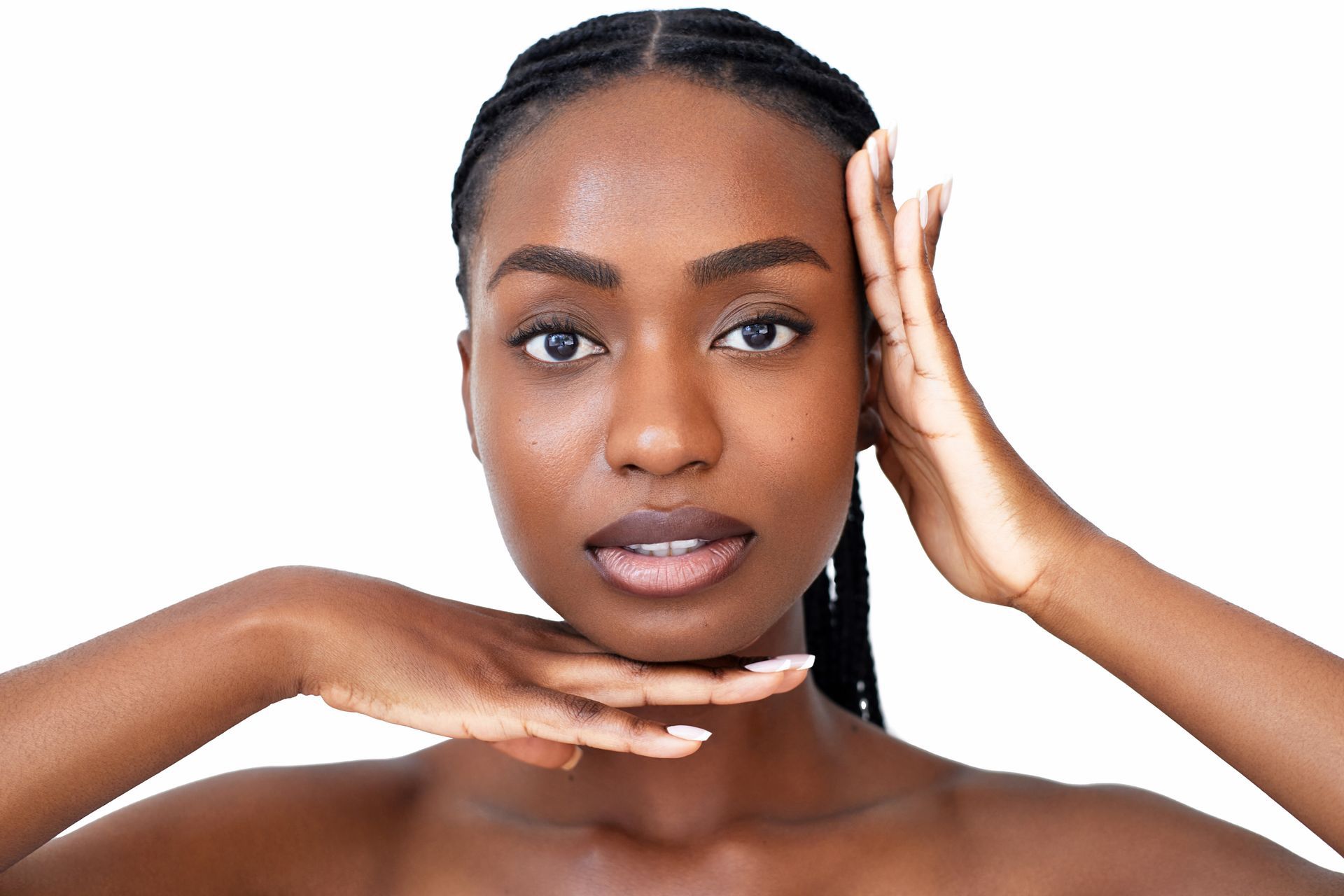 Portrait of a person posing with one hand on their cheek and one under their chin against a white background