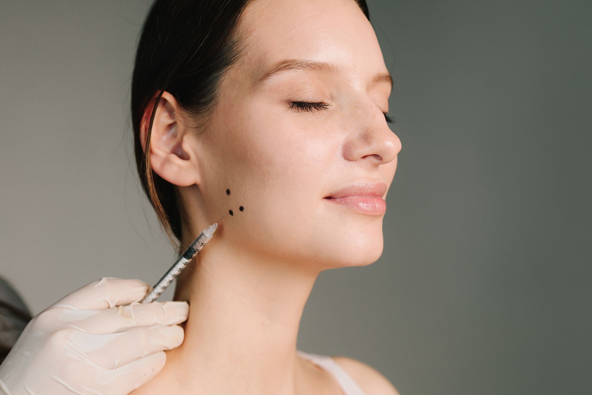 Woman receiving a cosmetic injection on her cheek against a gray background