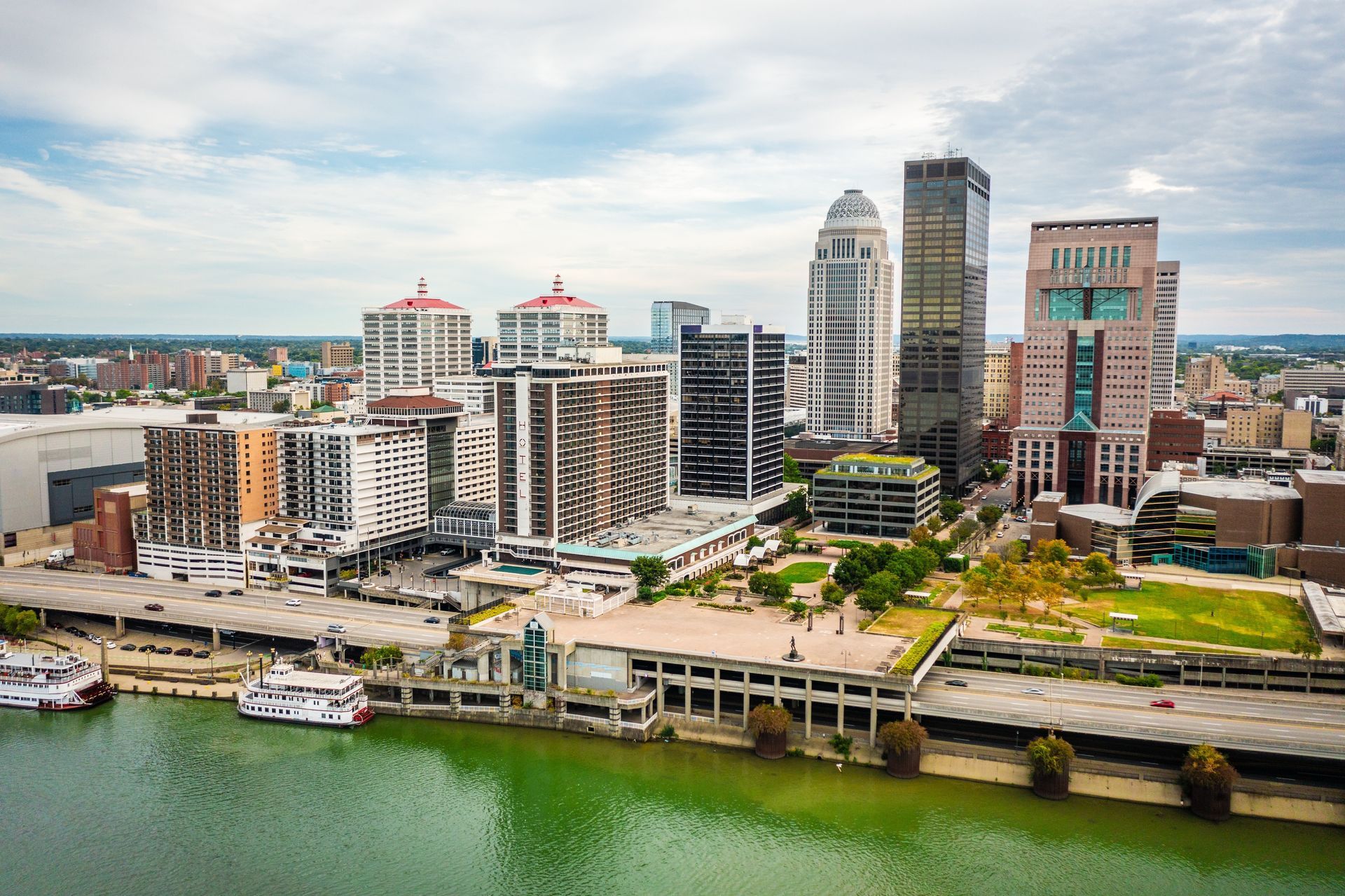 View of Louisville, Kentucky skyline, with skyscrapers, riverfront, and overcast sky.