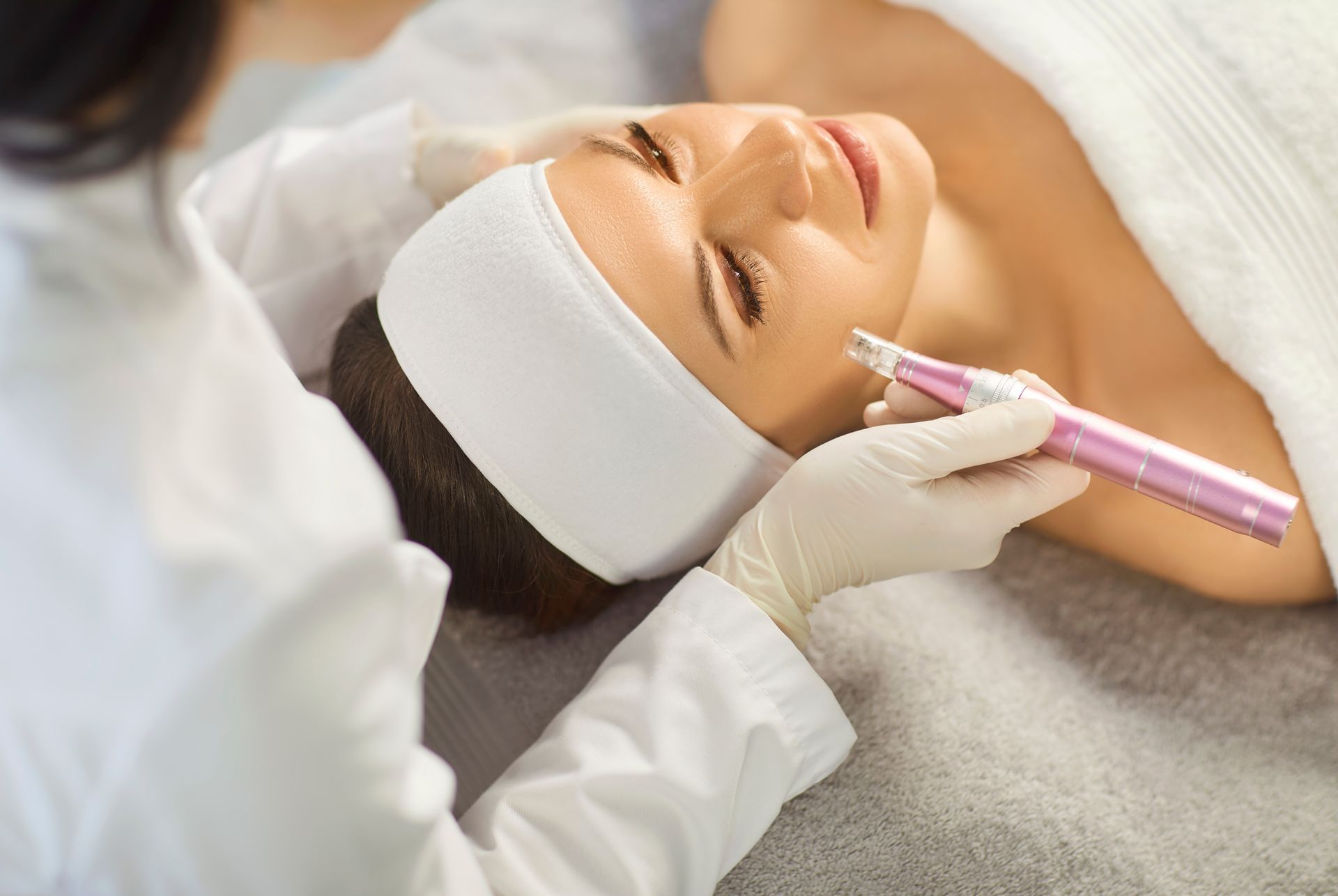 Woman receiving a facial treatment with a pink cosmetic tool on a spa bed