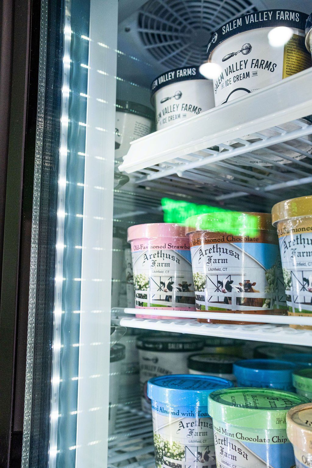 Shelves in a refrigerator display case filled with pints of Green Valley Farms ice cream.