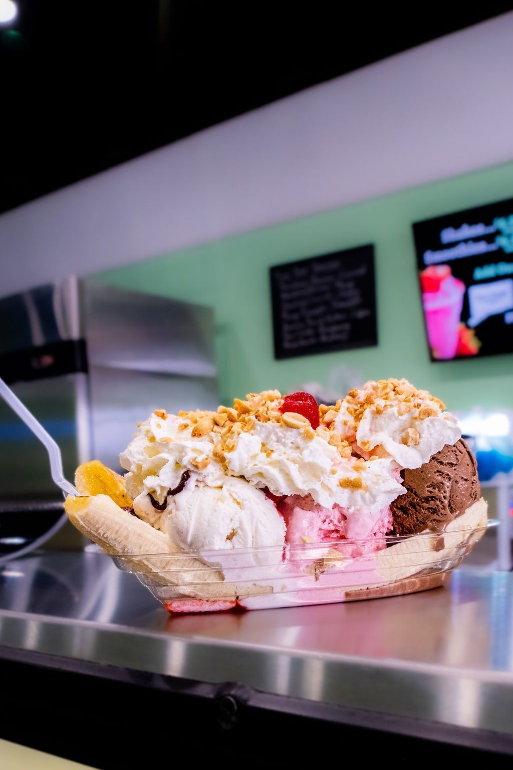 A banana split with three scoops of ice cream, whipped cream, nuts, and a cherry, served on a counter in a shop.