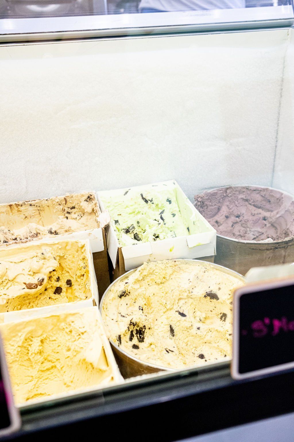 An ice cream display case containing multiple tubs of various flavors, including chocolate, mint, and s'mores.