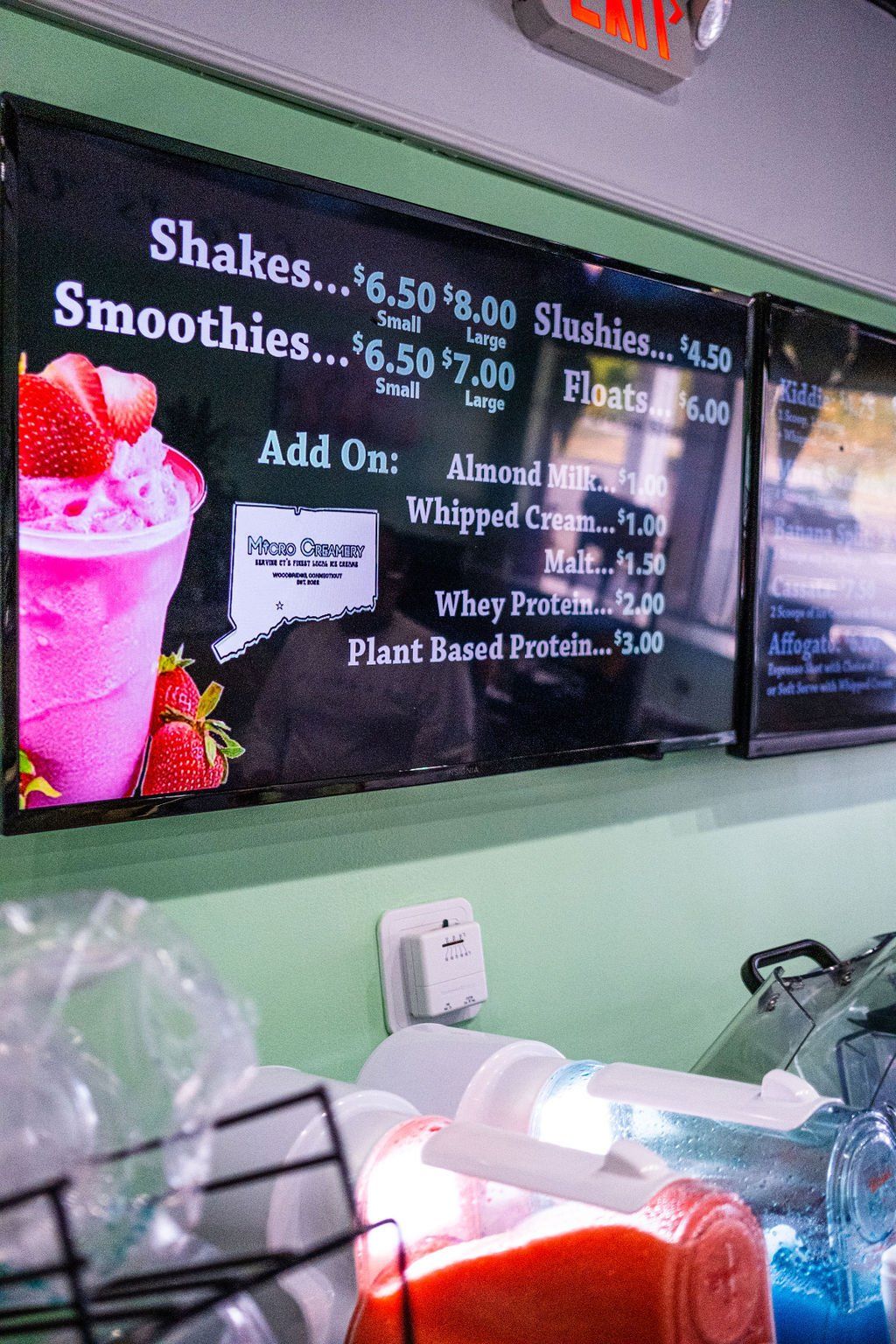 A menu board for a smoothie shop listing prices for shakes, smoothies, slushies, and various add-ons.