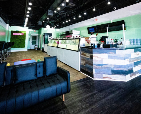 A modern storefront interior with a blue sofa in the foreground, a service counter, and a green plant-covered wall.