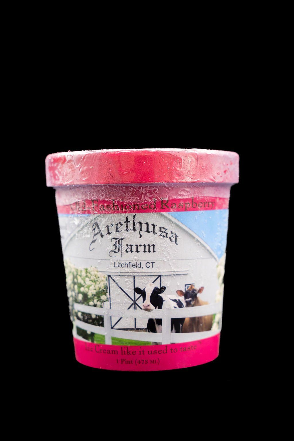 A pint container of Arethusa Farm ice cream with a white barn, cows, and a bright pink lid and bottom band on a black background.