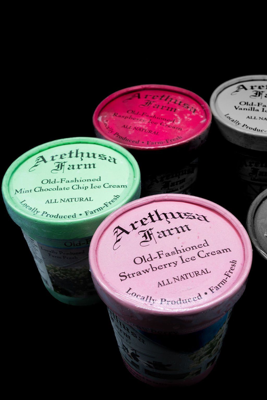 Four colorful cartons of Arethusa Farm Old-Fashioned Ice Cream arranged on a dark background.