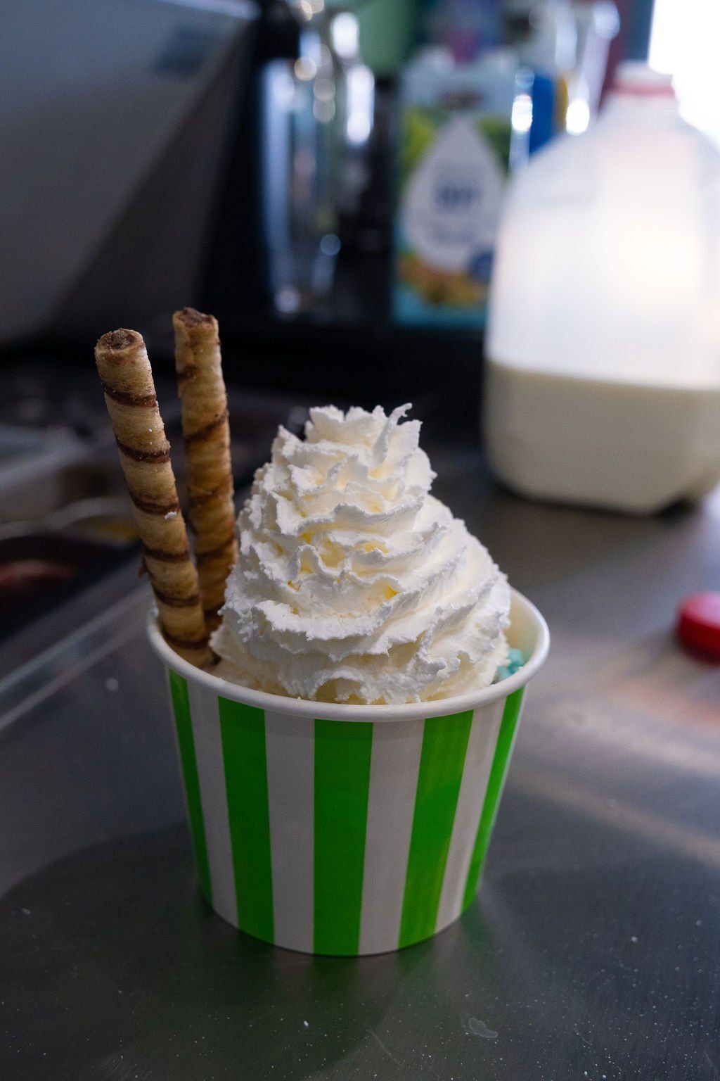 A cup of ice cream topped with whipped cream and two chocolate wafer rolls, sitting on a counter.