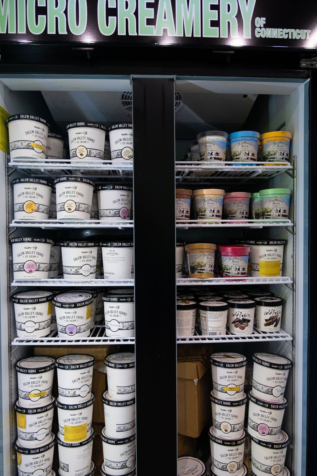 A display freezer stocked with shelves of various flavors of Micro Creamery of Connecticut ice cream pints.