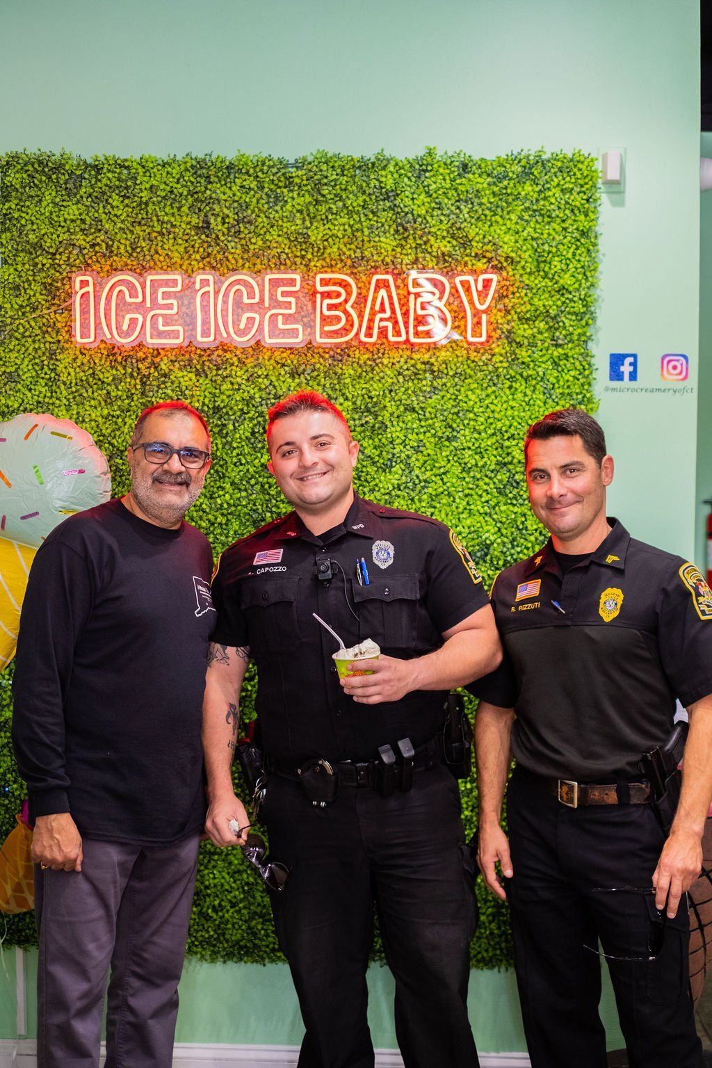 A man and two uniformed police officers smiling in front of a green wall with an 