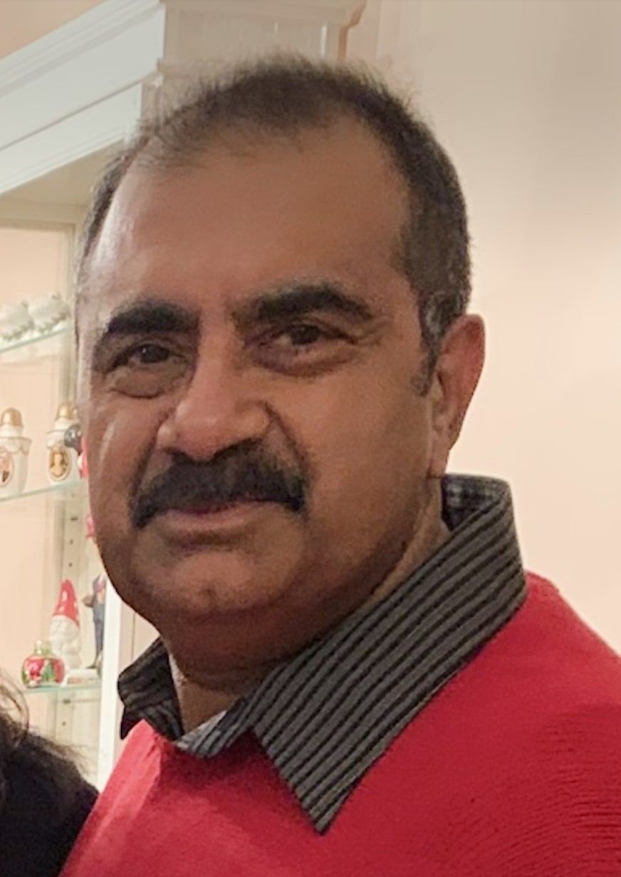 Co-owner of Micro Creamery, wearing a red sweater and a grey-striped collared shirt, posing indoors.
