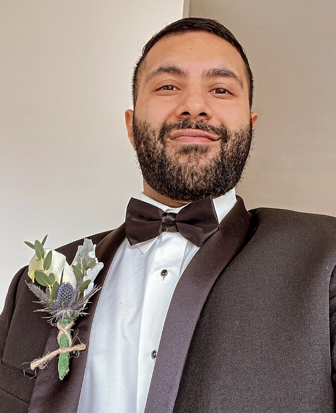 Co-Owner of Micro Creamery, wearing a dark suit, white shirt, and bow tie with a floral boutonniere pinned to the lapel.