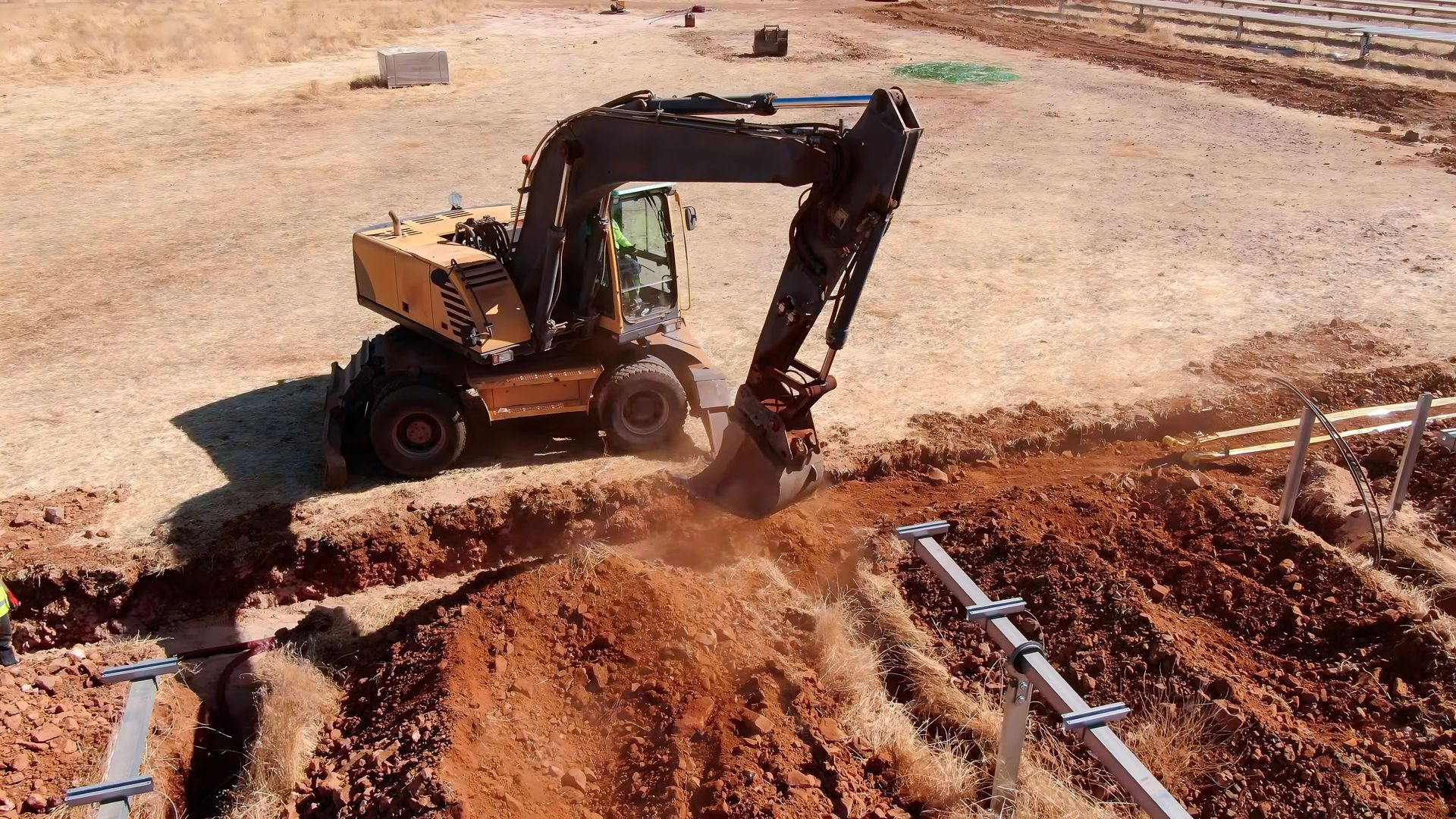 An excavator digging a trench in a construction site with brown soil.