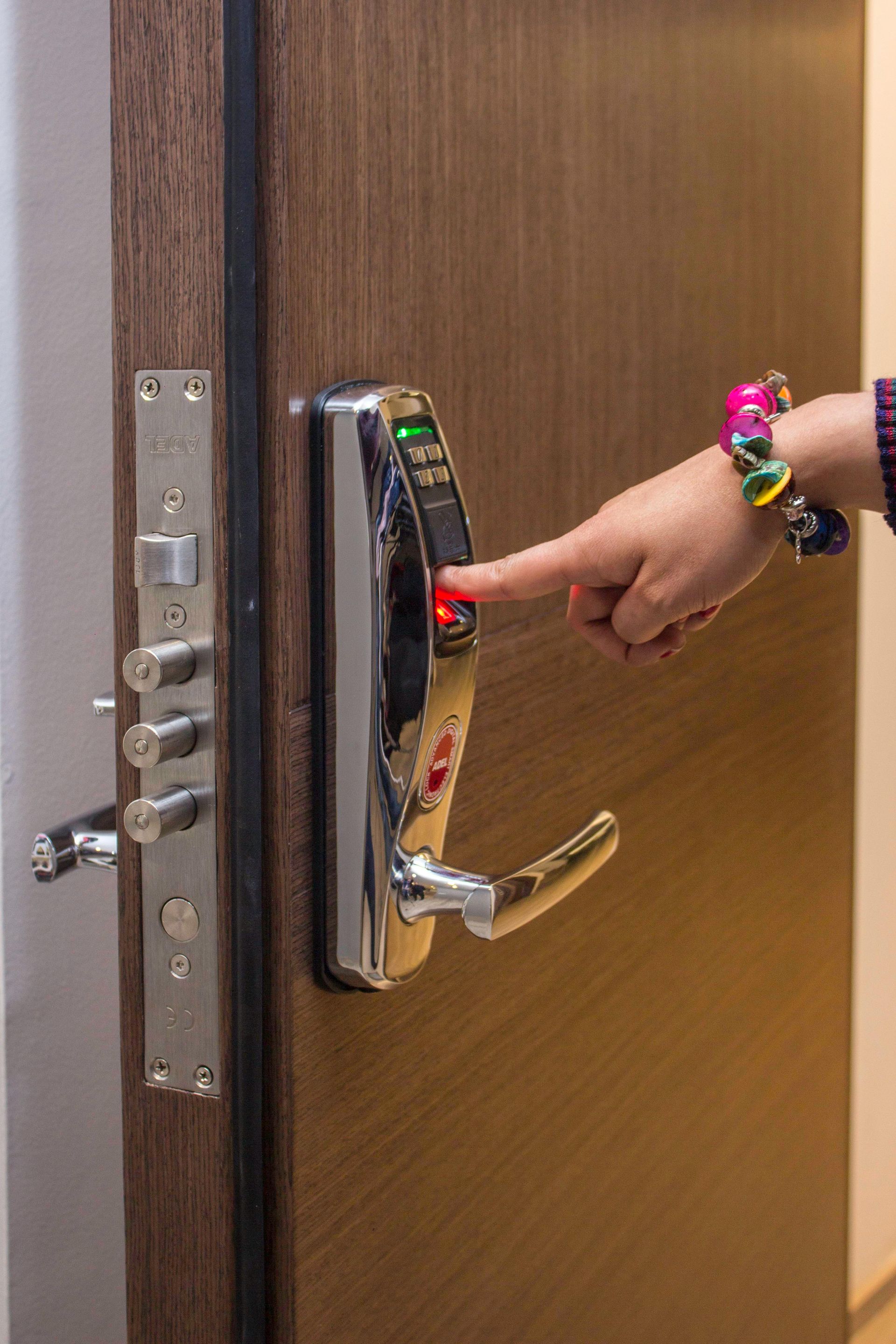 Hand pressing a red button on a chrome electronic door lock. Brown wooden door with a silver metal door latch.