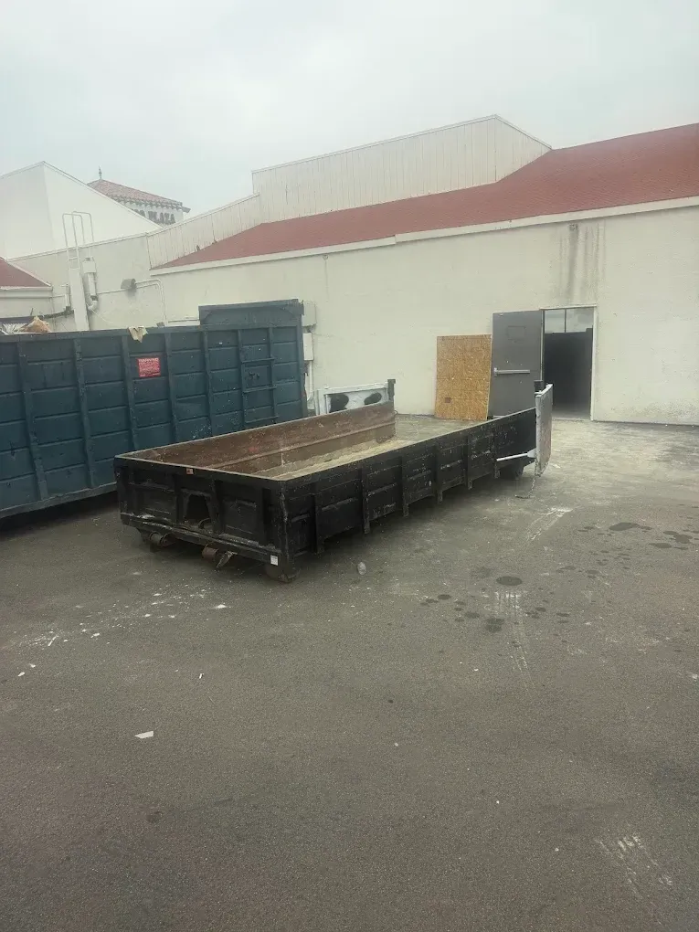 A black dumpster is sitting on top of a white surface.