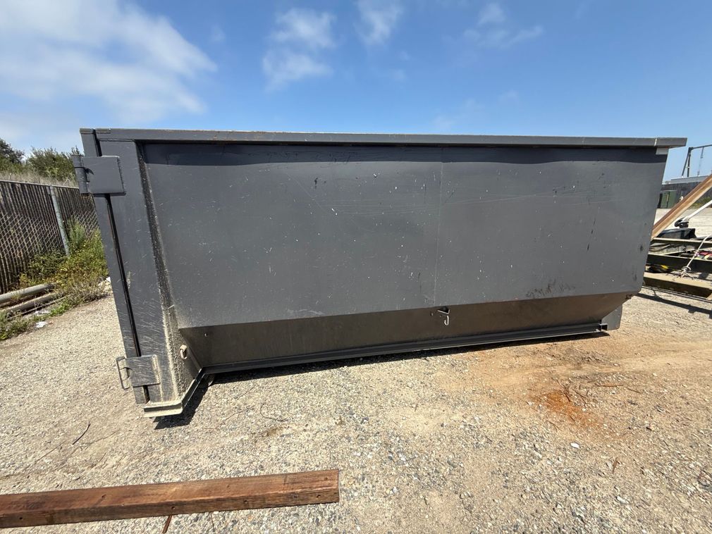 A black dumpster is sitting on top of a white surface.