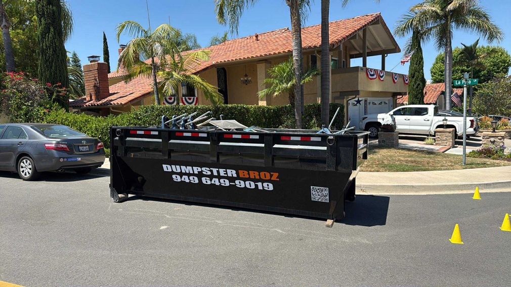 A black dumpster is sitting on top of a white surface.
